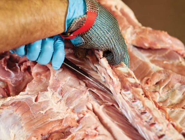 Mani con guanto in maglia metallica che disossano la carne di maiale