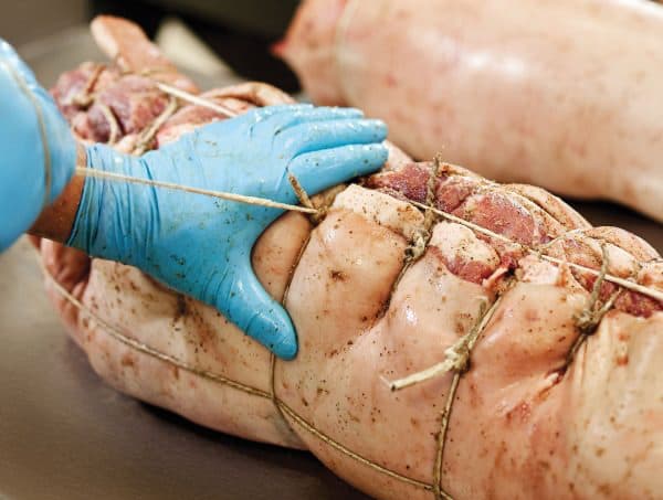 Mani che legano con lo spago il rotolo di porchetta
