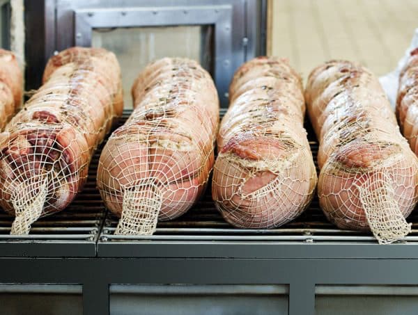 Porchette avvolte nella rete allineate sui carrelli del forno