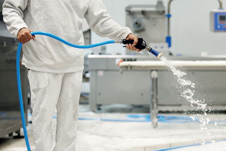 Operatore in tuta bianca sanifica con un getto d’acqua il pavimento della sala di lavorazione